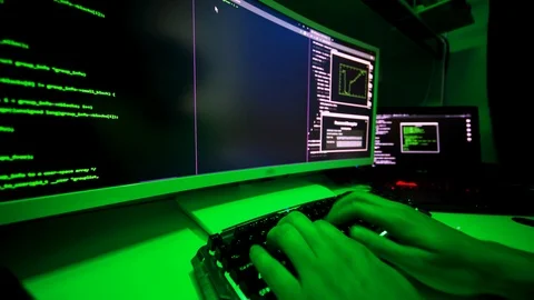 Hacker's hands on keyboard typing malicious code on large screen. Stockbeeldmateriaal 116897882