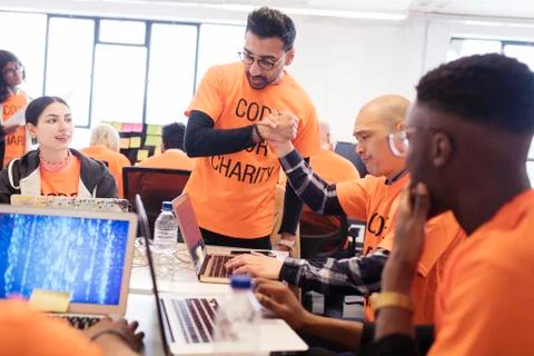 Hackers handshaking, celebrating and coding for charity at hackathon Stock Photos