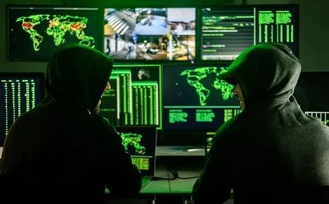 Hackers working on computers showing world maps and security camera footage Foto stock