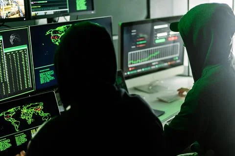 Hackers working on computers showing world maps and security camera footage Foto stock