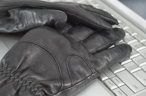 Hacking concept with pair of black leather gloves over metallic laptop keyboa 스톡 사진