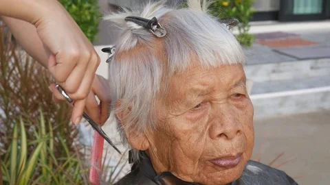 Hair stylist cutting senior woman's gray hair Stock Footage