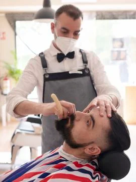 Hairdresser grooming beard at barber shop to a client, both wear maskhairdres Stock Photos