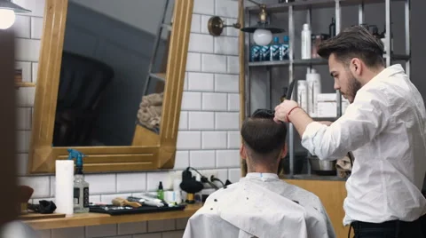 Hairstyling process. Close-up of a barber drying hair of a young bearded man Stock Footage 68058145