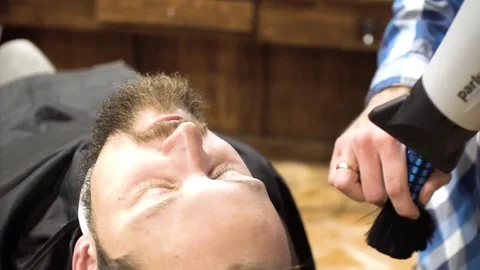 Hairstyling process. Close-up of a barber drying hair of a young bearded man Stock Footage 69989493