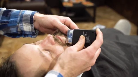 Hairstyling process. Close-up of a barber drying hair of a young bearded man Stock Footage 69989950