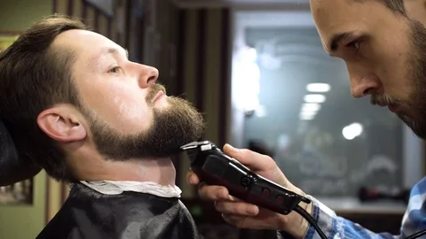 Hairstyling process. Close-up of a barber drying hair of a young bearded man Stock Footage 69990755