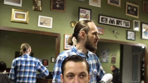 Hairstyling process. Close-up of a barber drying hair of a young bearded man Stock Footage 69990941