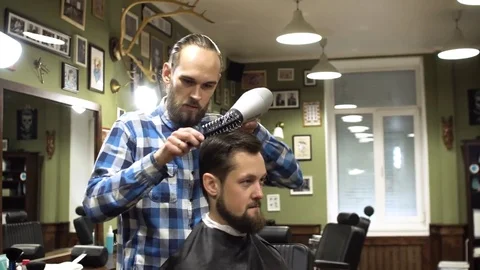 Hairstyling process. Close-up of a barber drying hair of a young bearded man Stock Footage 69991116