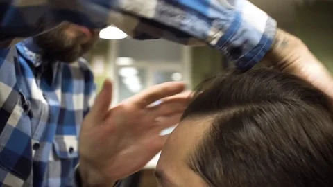 Hairstyling process. Close-up of a barber drying hair of a young bearded man Stock Footage 69991354