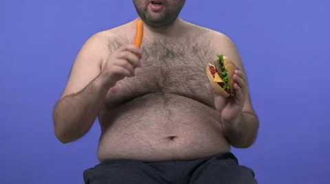 Hairy overweight man choosing between carrot and hamburger. He chooses carrot. Stock Footage 45926184