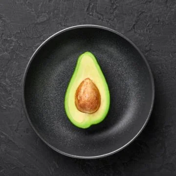 Half Avocado in black rough ceramic bowl on dark slate backdrop.  Stock Photos