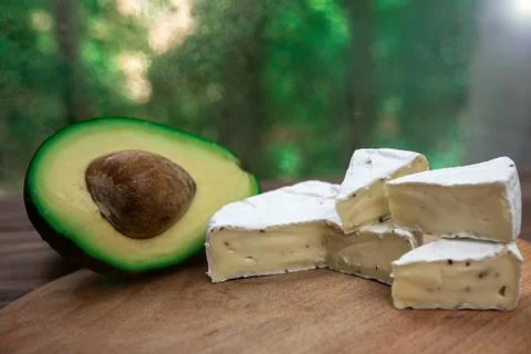 Half avocado with bone and slices of brie cheese or camembert with mold Stock Photos