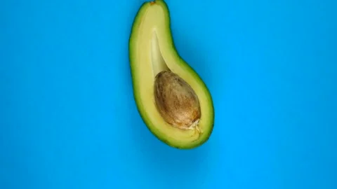 Half avocado fruit fast rotating on blue table. Avocado is a highly nutritious Stock Footage 166740001