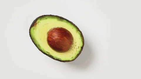 Half an avocado with a pit is spinning on a white background Stock Footage 248912305