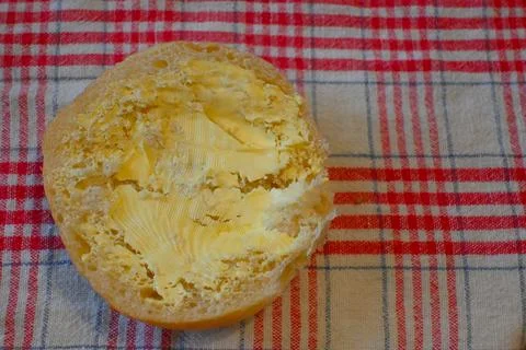 Half bread roll with margarine on checkered cloth Fotos de archivo