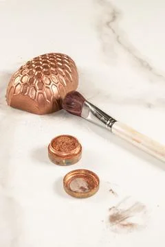 Half a chocolate Easter egg next to a paintbrush and edible copper powder ver Stock Photos