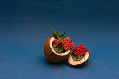 Half of coconut with ruby chocolate pieces inside decorated with basil. Blue Stock Photos