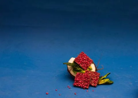 Half of coconut with ruby chocolate pieces inside decorated with basil. Blue Stock Photos