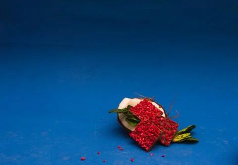 Half of coconut with ruby chocolate pieces inside decorated with basil. Blue Stock Photos