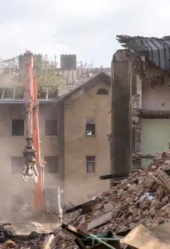 Half collapsed brick house covered in dust and debris with a crasher machine Stock Photos