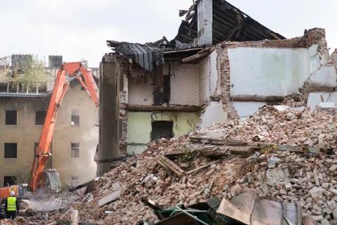 Half collapsed brick house covered in dust and debris with a crasher machine Stock Photos