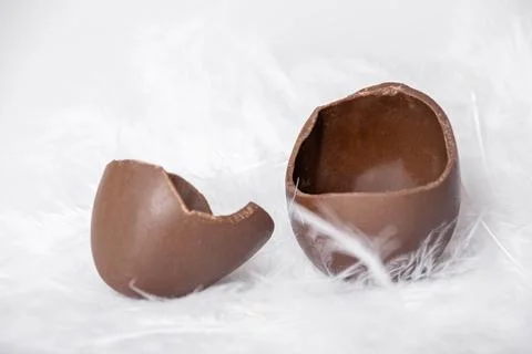 Half of a cracked empty chocolate egg and empty egg shell in nest of white fe 스톡 사진