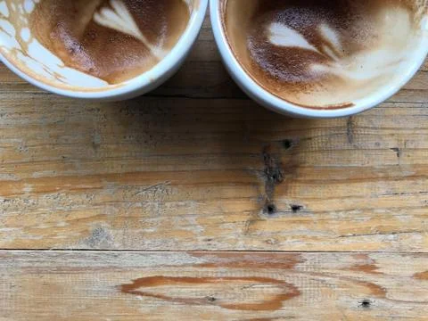 Half cups of two finished hot latte coffee with leftover latte art on wood table Stock Photos