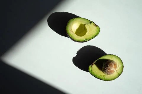 A half-cut avocado lies on the table top view, bright sunlight, hard shadows  Stock Photos