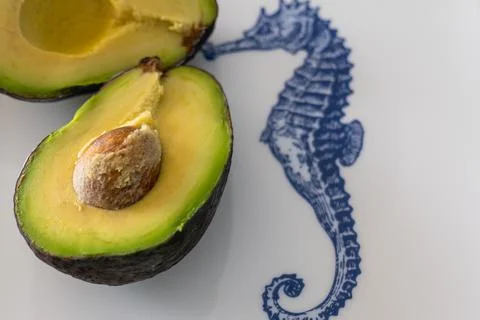 Half cut avocado with seed pit, stone, on a white plate with sea horse print Stock Photos