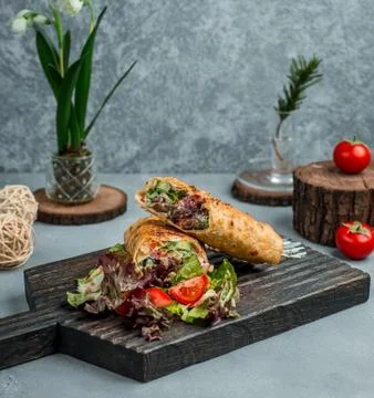 Half cutted fried beef burrito with cucumber, tomato, lettuce, mayonnaise on Stock Photos