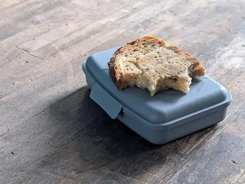 Half eaten slice of rustic bread resting on blue lunchbox on wooden table Fotos Stock