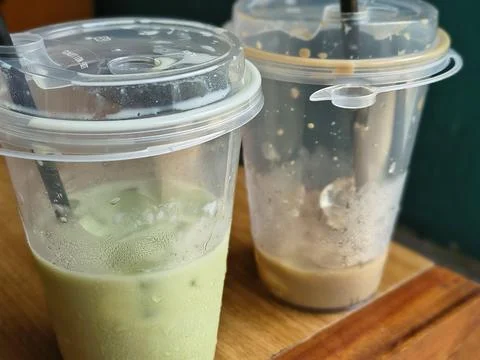 A half empty cup of iced coffee and matcha latte in a transparent plastic cup Stock Photos