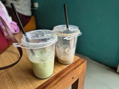 A half-empty cup of iced coffee and matcha latte in a transparent plastic cup Stock Photos