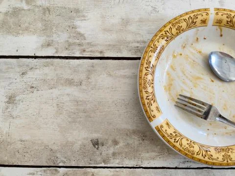 Half empty dirty plate with fork and spoon on rustic wooden table background Stock Photos