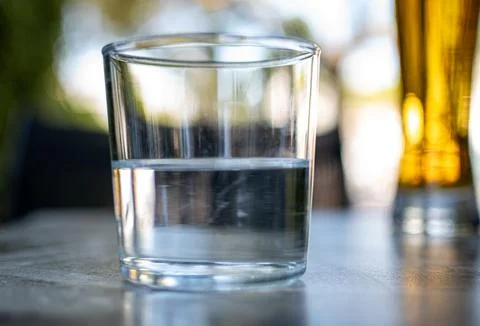 A half empty or a half full glass of water on a table. Stock Photos