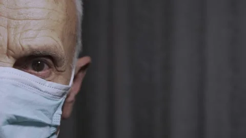Half face of elderly man in facemask against gray curtain at home Stock Footage 166795262