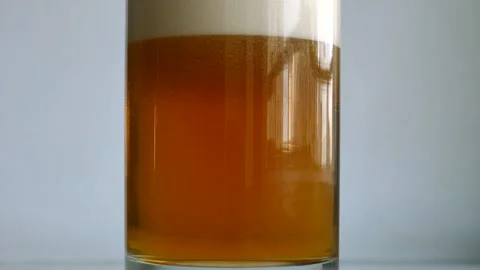 Half filled glass is filled with light beer to the top and forms a thick foam Stock Footage 297405981