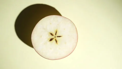 Half fresh apple rotating on the sunlight on a colored yellow background Stock Footage 222078740
