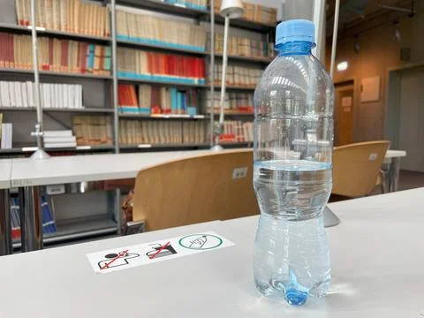 Half-Full Plastic Water Bottle on a Library Table With Bookshelves in the Fotos de archivo