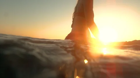 HALF IN HALF OUT: Surfer sits on her surfboard and waits in line up at sunrise Stock Footage 127429123