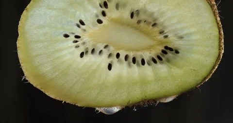 Half a kiwi on a black background with several drops of juice falling Stock Footage 144829865