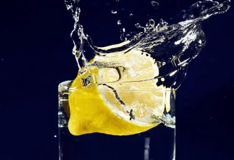 Half of lemon falling down in glass with water on deep blue Fotos Stock