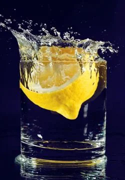 Half of lemon falling down in glass with water on deep blue Foto stock