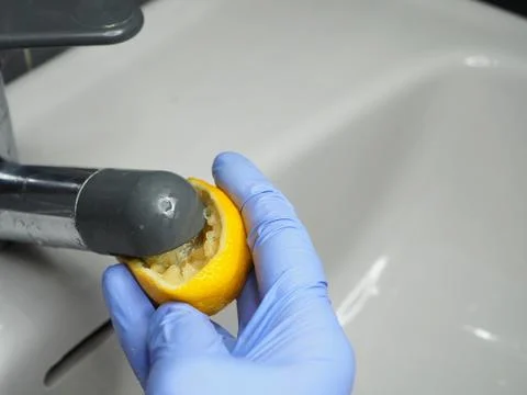Half a lemon, a gloved hand and a chrome faucet on the sink 库存照片
