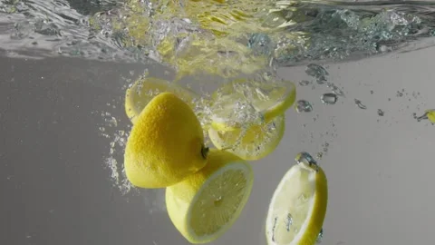 Half of lemons and lemon slices dropped into the transparent aquarium with water Stock Footage 133227855