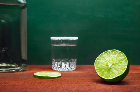 Half of a Lime with Blurred Lime Slice, Silver Tequila Shot Rimmed with Salt Stock Photos
