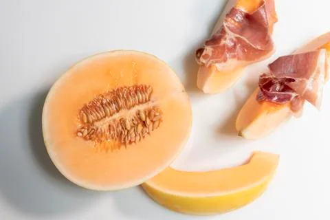 Half melon next to some slices with thin cured ham slices on top of them.Tast Stock Photos