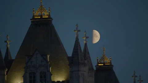 Half-moon above the lit Gothic spires of Tower Bridge at dusk. Видео 321607599