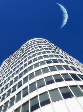 Half a moon over a building skyscraper, shining in bright blue sky. Below the 스톡 사진